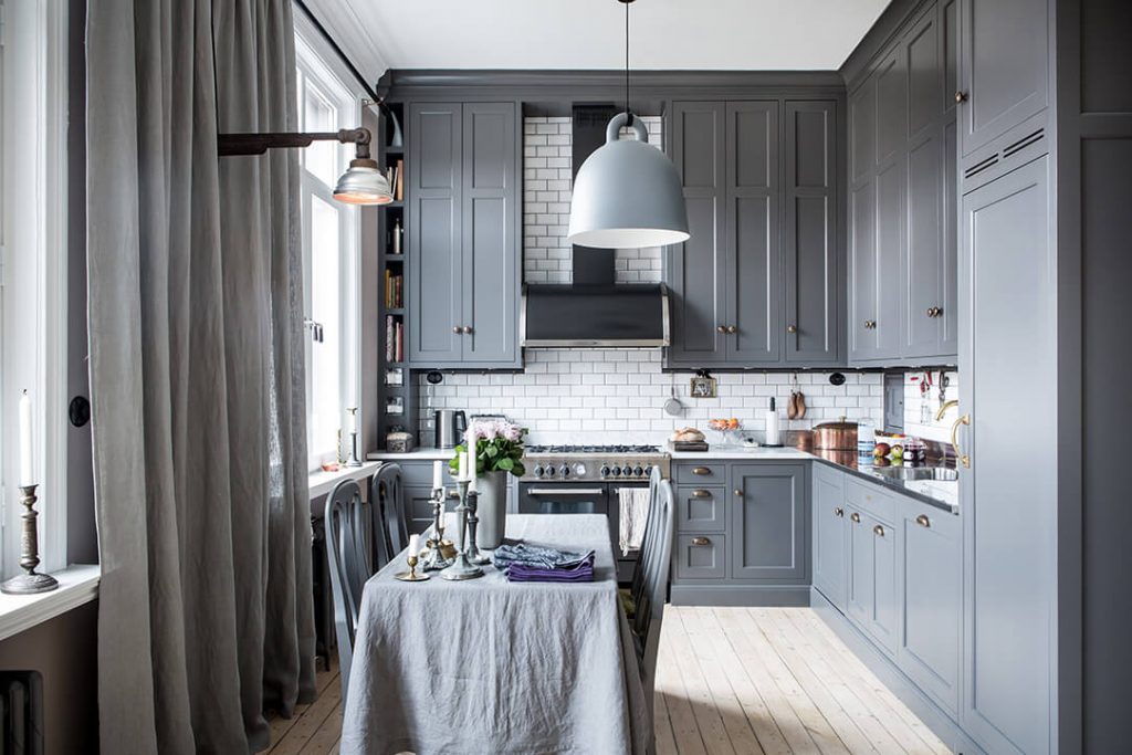 На кухне есть промышленные деревянные шкафы, окрашенные в серый цвет, с L-образным дизайном.