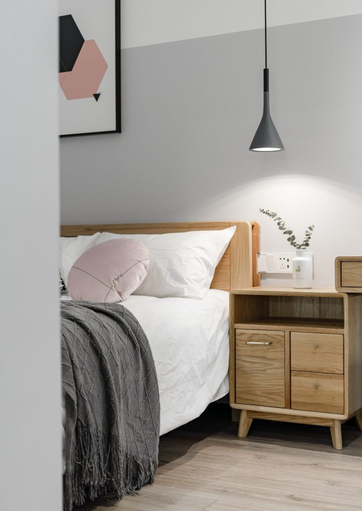Giường ngủ sử dụng bộ ga đệm trắng xám cùng đèn ngủ trang trí và tranh treo tường