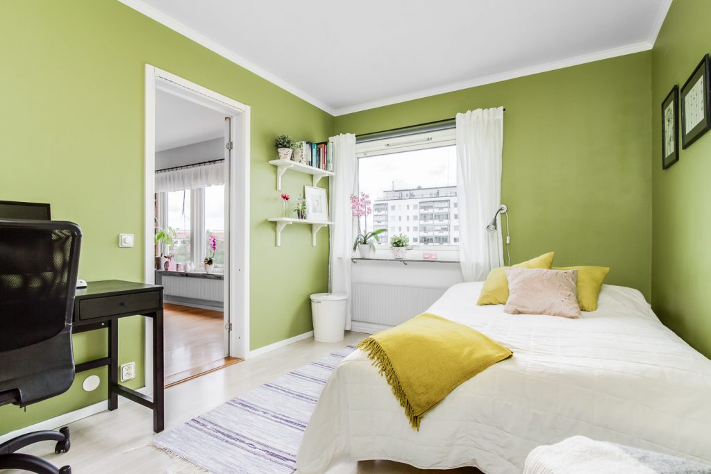 O quarto usa tons verdes e a cama tem lençóis brancos