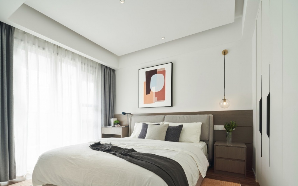Phòng ngủ chính thiết kế tối giản hóa nội thất có giường ngủ lớn, hai kệ tủ để đồ trang trí nhỏ, và tranh treo tường 