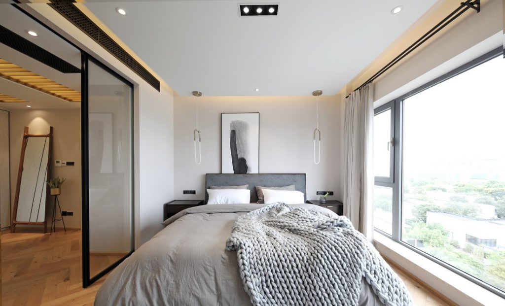 غرفة نوم رئيسية بتصميم داخلي على الطراز الاسكندنافي ، مع نوافذ كبيرة وستائر بيضاء