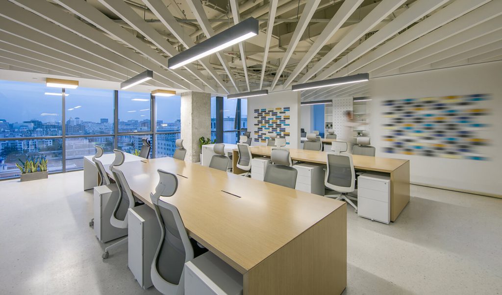 Khu vực làm việc của nhân viên rộng rãi, cùng bộ bàn ghế văn phòng hiện đại có tựa đầu, phía trên là đèn led 