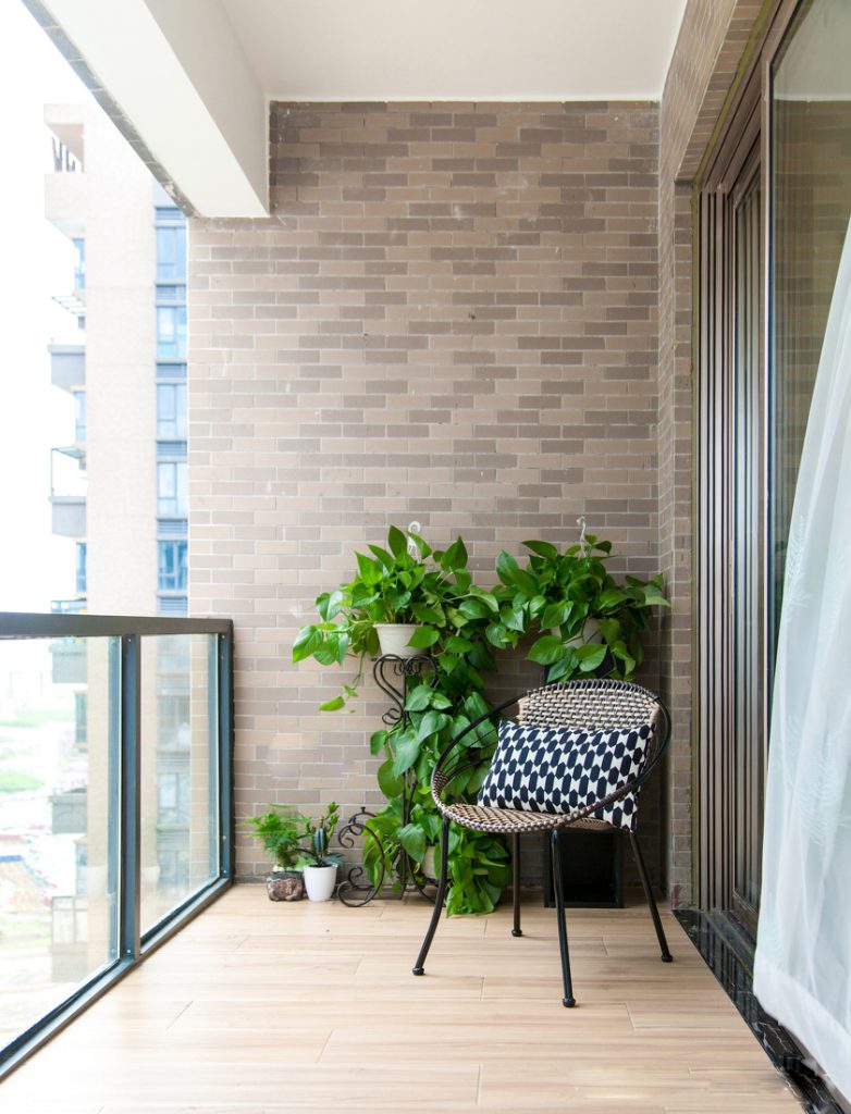شرفة مع كرسي كسول وأواني نباتات خضراء وأرضية خشبية وحاجز زجاجي
